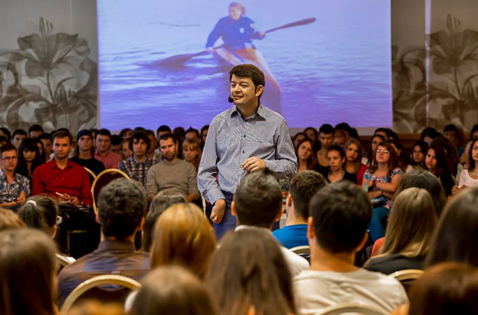 Un speaker cu dizabilitate vorbește în fața unei săli pline de oameni