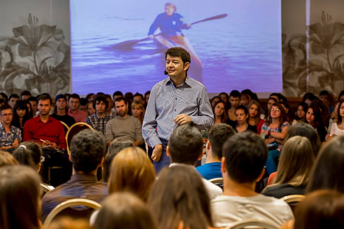 Un speaker cu dizabilitate vorbește în fața unei săli pline de oameni