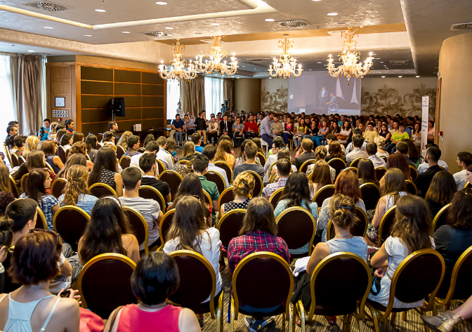 O sală plină de oameni care ascultă discursul unui speaker