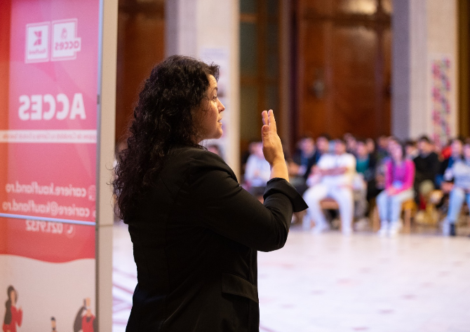 O femeie ține un discurs în fața unui public.  