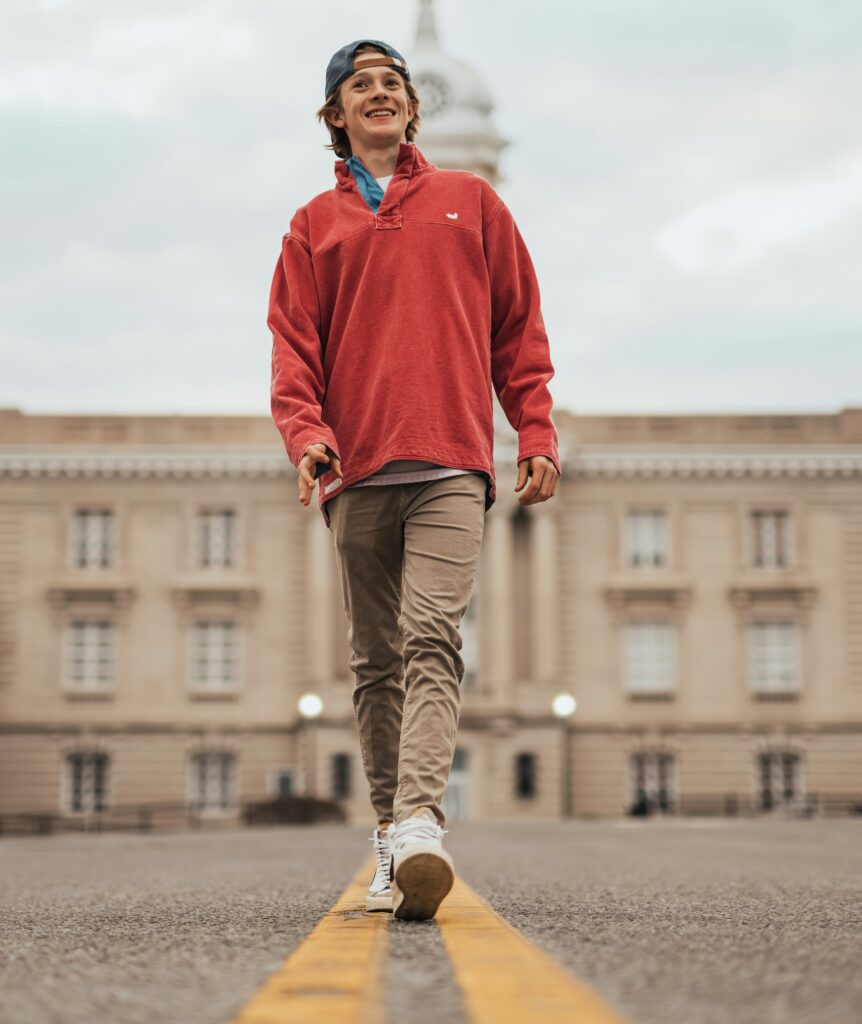 Băiat purtând un hanorac roșu se plimbă în fața unei clădiri 