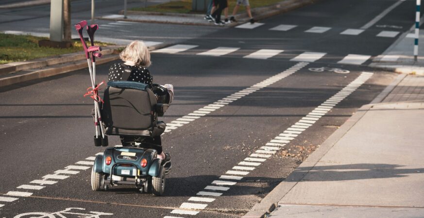 Femeie în scaun rulant se deplasează pe stradă.