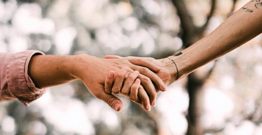 Două persoane se țin de mână undeva în natură.