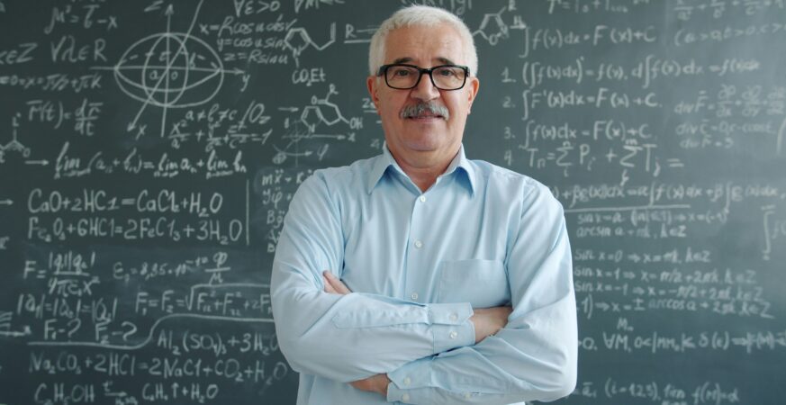 Bărbat în vârstă stă cu spatele la o tablă plină de formule matematice