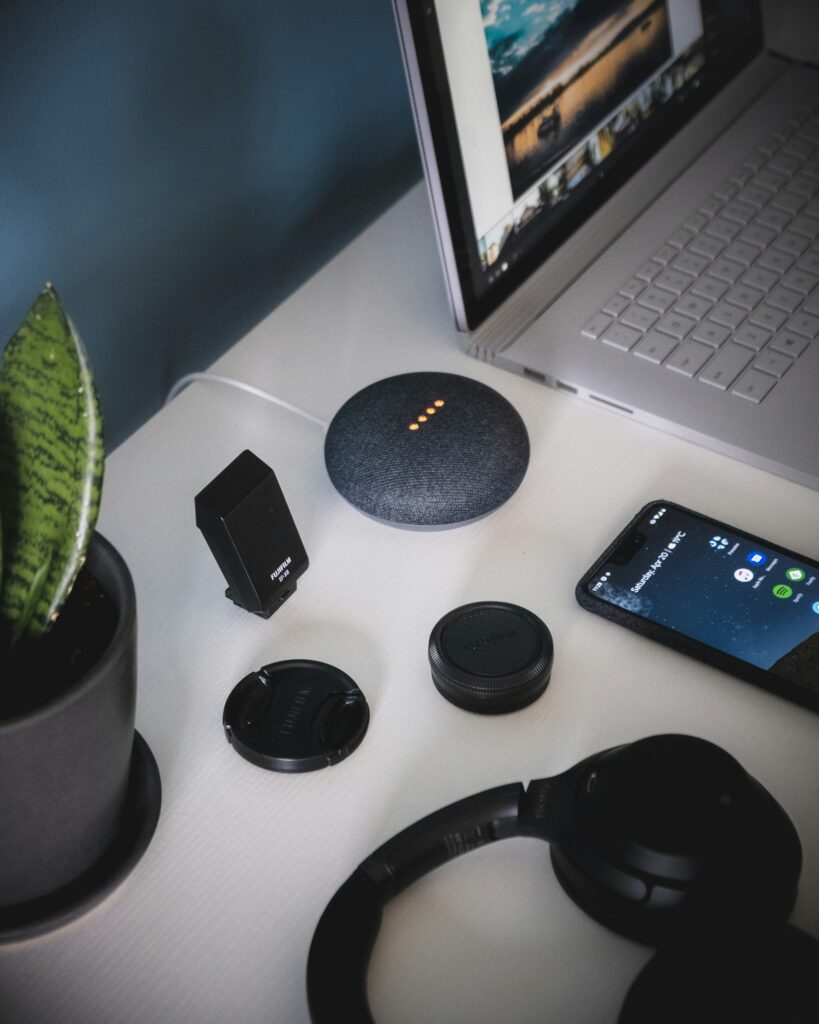 Pe un birou sunt așezate un laptop, un telefon, un asistent vocal inteligent Siri, căști, boxe și alte obiecte mici. 