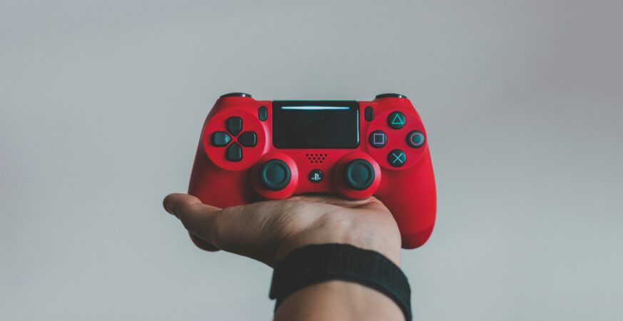 O persoană ține în mână o telecomandă wireless roșie pentru jocuri video.