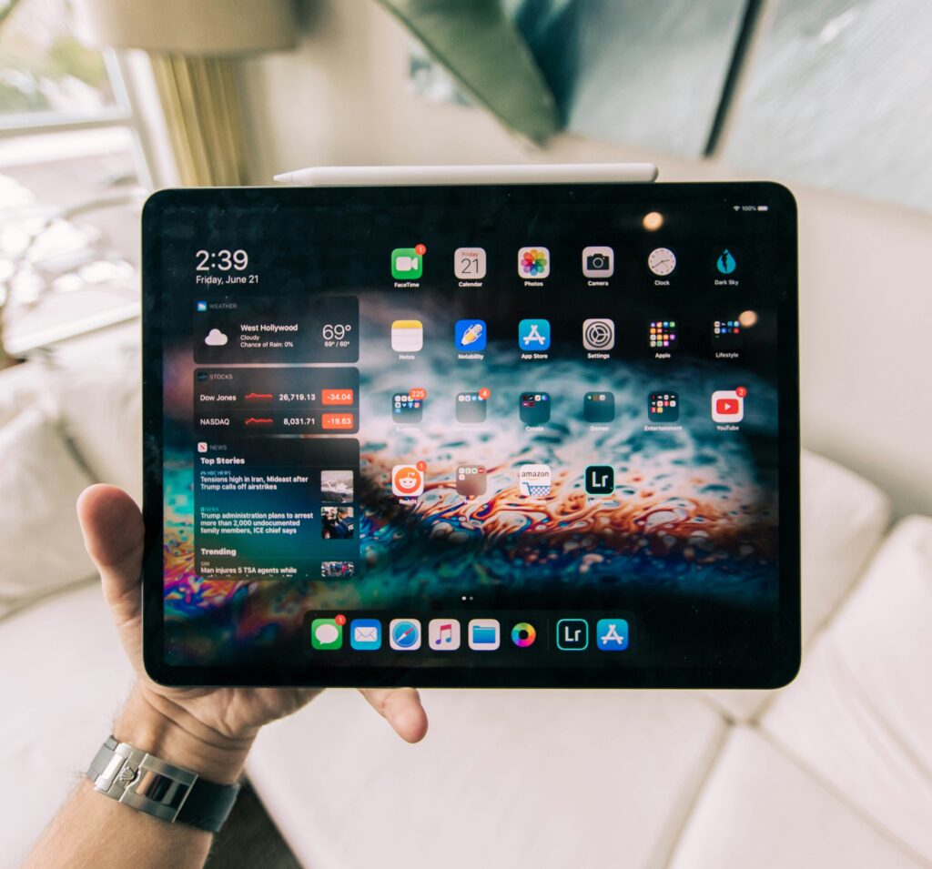 O persoană ține în mână o tabletă cu ecranul pornit, pe ecran fiind vizibile diverse aplicații și mesaje. 