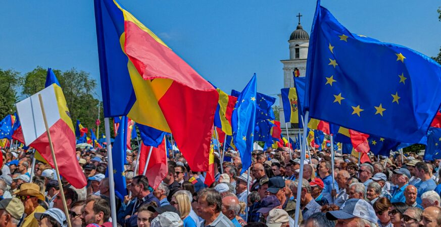 O mulțime de oameni într-un spațiu deschis, purtând steaguri ale României și UE.